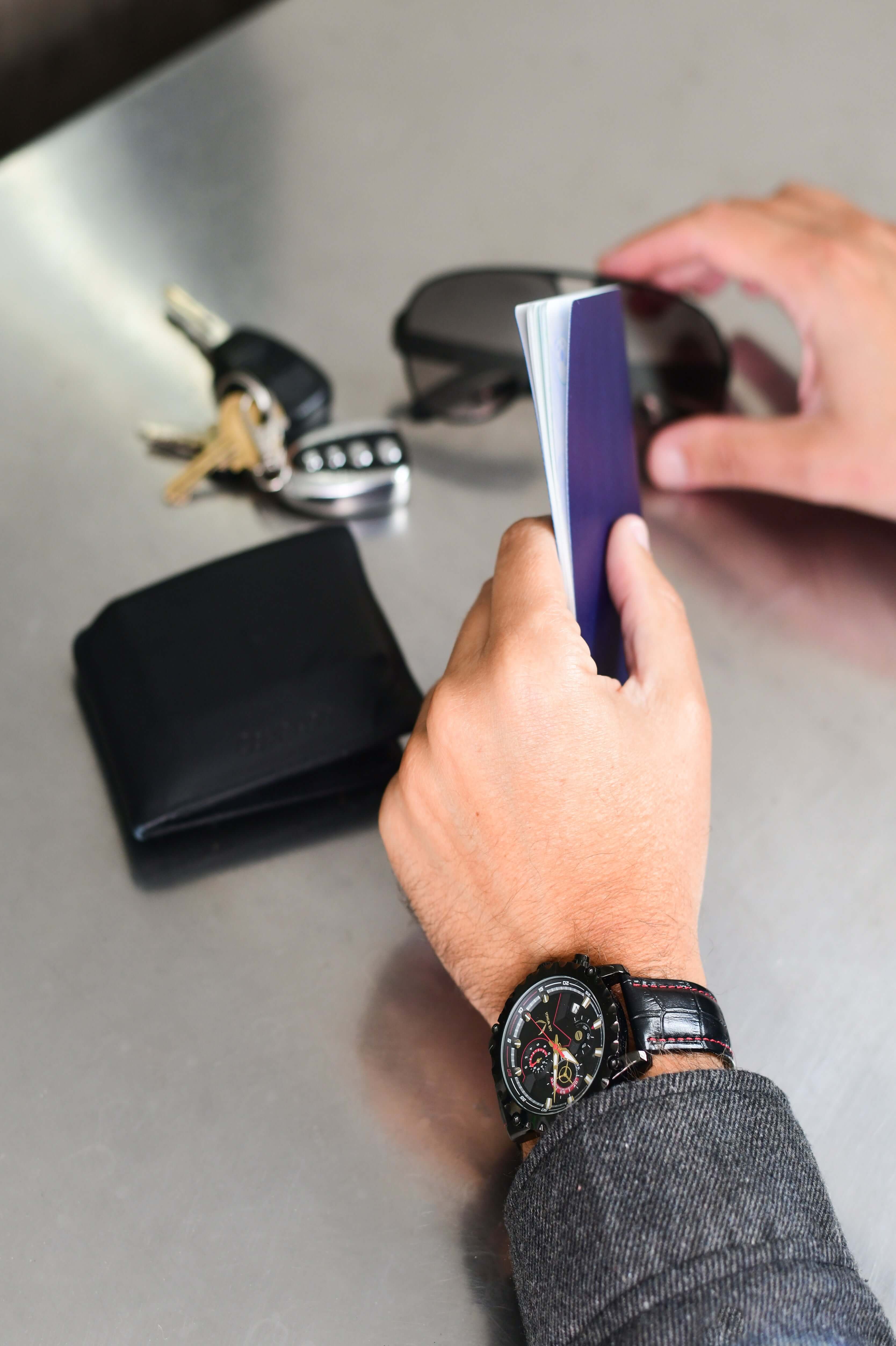 A hand holding a notebook with Air Wings Ace - Gold/Black watch, keys, and sunglasses on a table.